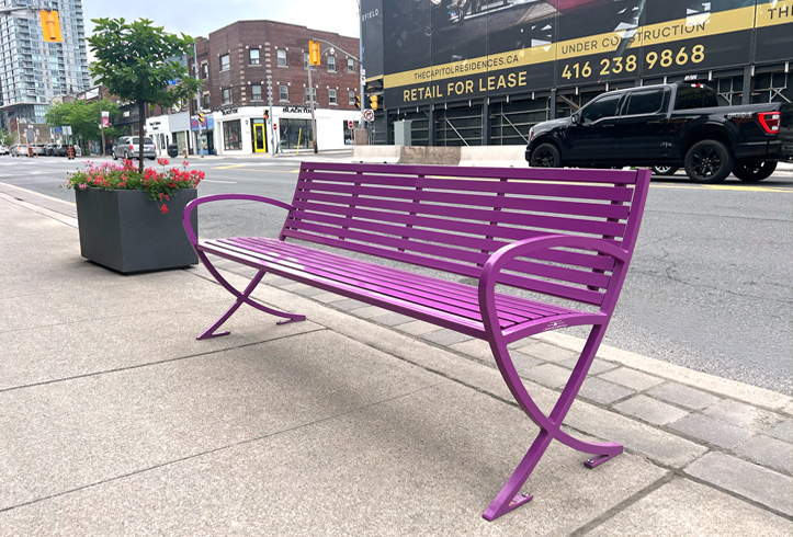 A brightly coloured Victor Stanley bench on a streetscape in a Toronto business improvement area.